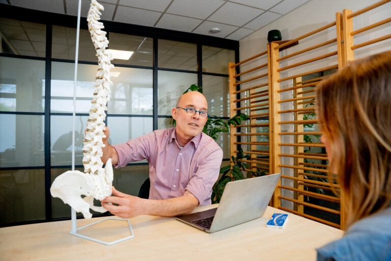 Specialist legt scoliose uit aan kind en ouder met behulp van een wervelkolommodel